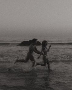 two people running in the water at the beach