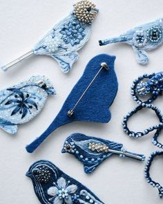 blue bird brooches and pins are arranged on a white surface with beading