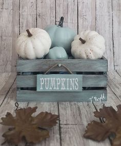 a wooden crate filled with pumpkins on top of a wooden floor next to leaves