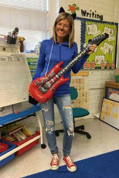 a woman holding a red guitar in front of a whiteboard with writing on it