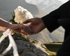 the bride and groom are holding hands on top of a mountain with their wedding bouquet