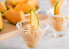 two glasses filled with food sitting on top of a wooden tray next to melon slices