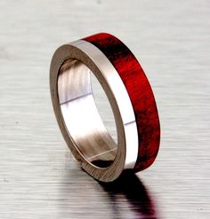 a wooden ring with silver and red inlays sits on a shiny surface as if it were made out of wood