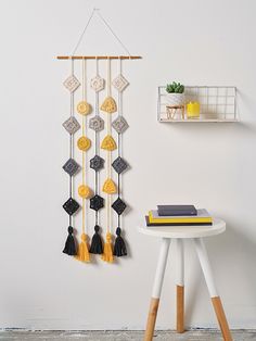 a wall hanging with tassels on it next to a small table and shelf