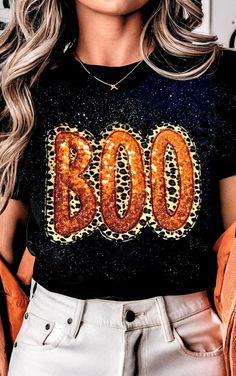 This BOO-tiful bold Halloween tee is a spooky-chic statement piece! The word "BOO" is spelled out in striking orange sequins with leopard-print accents adding a touch of wild style! Unique bleach-splatter design gives it a cool, edgy vibe! A fun and glamorous piece to add to your autumn wardrobe! Super soft unisex tee. True to size. SM 2/4, MED 6/8, LRG 10/12, XL 14/16, 2X 18/20, 3X 22/24 FREE SHIPPING! Fall Party Tops With Letter Print, Fall Letter Print Party Tops, Letter Print Tops For Fall Parties, Halloween Party Tops With Letter Print, Black Party T-shirt For Fall, Black T-shirt For Fall Party, Halloween Party Letter Print Tops, Fall Leopard Print Tops With Letter Design, Fall Leopard Print Top With Letter Details