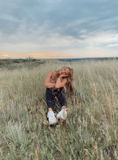 a woman sitting in the middle of a field with her head on her hands and eyes closed