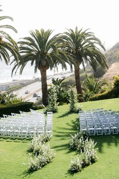 an outdoor ceremony set up with white chairs and palm trees in the foreground, overlooking the ocean