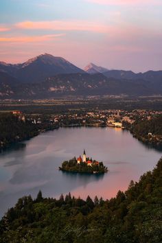 a small island in the middle of a lake surrounded by trees and mountains at sunset