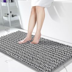 a person standing on a bathroom rug in front of a bathtub with rocks all over it