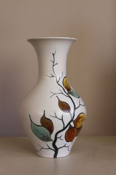 a white vase sitting on top of a table with leaves painted on the side of it