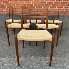 six wooden chairs with woven seat cushions on the ground next to a brick wall and sidewalk