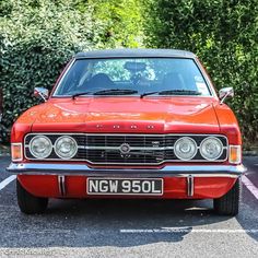 an orange car parked in a parking lot next to some bushes and trees with the number plate ngw90l