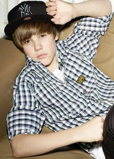 a young man sitting on top of a brown couch wearing a black and white hat