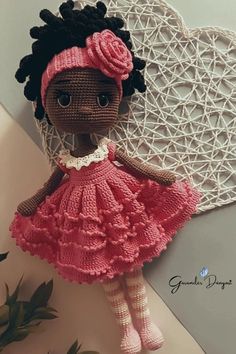 a crocheted doll with a pink dress and headband sitting on a table