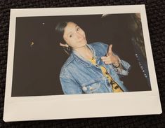 a polaroid photo of a woman giving the thumbs up sign while wearing a denim jacket