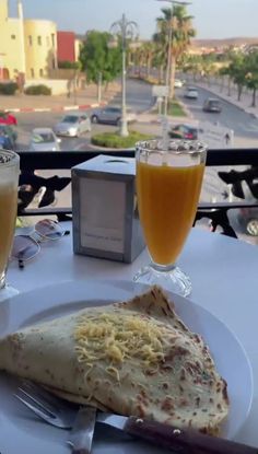 two glasses of orange juice and an omelet on a white plate with silverware