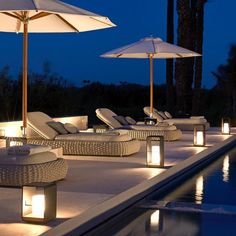 lounge chairs and umbrellas next to a pool at night