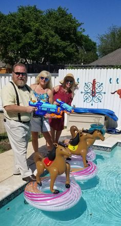 two women and a man standing next to an inflatable pool with horses on it