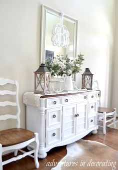 a white dresser sitting next to a mirror on top of a wooden floor in a room