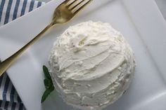 a white plate topped with a cake covered in frosting and a gold fork next to it