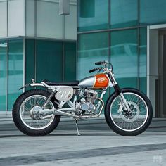 an orange and silver motorcycle parked in front of a tall building with glass windows on the side