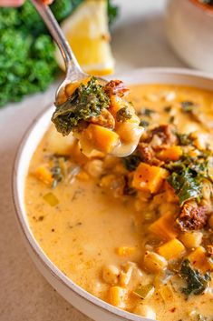 a spoon full of soup with broccoli and other foods in the bowl next to it