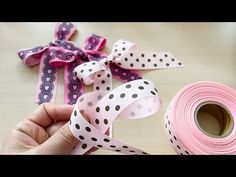 a person holding a pink ribbon with black dots on it next to two rolls of tape