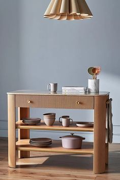 a wooden table with plates and cups on it in front of a light fixture hanging from the ceiling