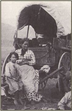 an old black and white photo of two women sitting in front of a covered wagon