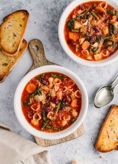 two bowls of pasta soup with bread on the side