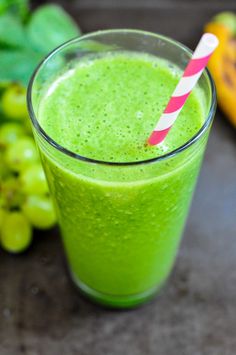 a green smoothie with a red and white striped straw in front of some grapes