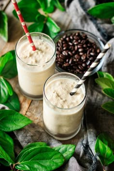 two glasses filled with milk sitting on top of a wooden table next to green leaves