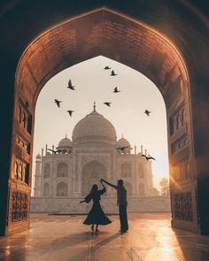 two people standing in front of an arch with birds flying around them and one person holding the other's hand