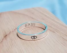 a ring with two hearts engraved on it sitting on top of a wooden table next to a blue background