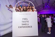 a group of people standing around a sign that says feel taste smell experience