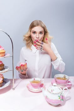 a woman sitting at a table with cupcakes and tea cups in front of her