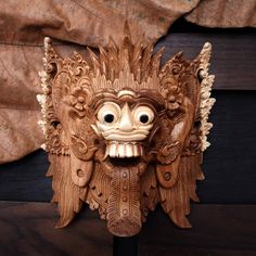 a carved wooden mask on a stand with eyes wide open and mouth wide open, in front of a curtain