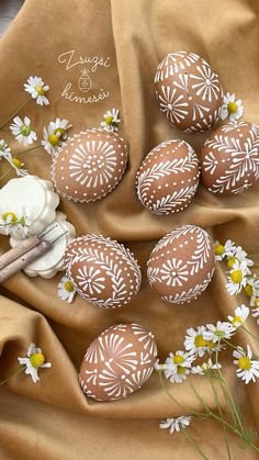 some white and brown decorated eggs with daisies on a tan cloth next to flowers