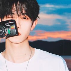 a young man holding up a camera to his face with the sky in the background