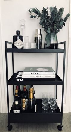 a black shelf with bottles and glasses on it next to a vase filled with flowers