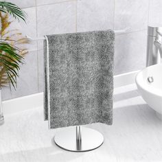 a towel is hanging on a stand in the bathroom next to a sink and potted plant