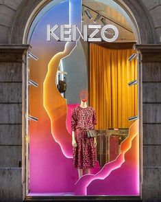 a mannequin dressed in a red dress is standing behind a display window with the words kenzo on it