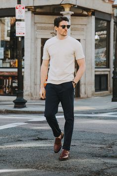 a man in white shirt and black pants walking across the street with his hand on his hip