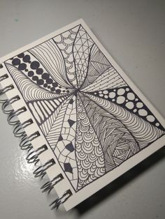 an open spiral notebook with black and white designs on it, sitting on a table