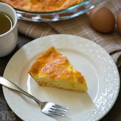 a slice of quiche on a plate next to a cup of tea and an egg