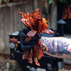 a person holding up some bacon in their hand with tattoos on his arm and arms