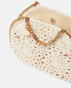 a white crocheted purse with gold chains on the handle and chain at the bottom