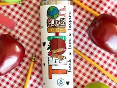 an apple and some pencils on a checkered table cloth with apples in the background