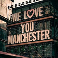 we love you manchester sign in front of a building with lots of lights on it