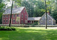 a large red house sitting in the middle of a lush green field next to trees